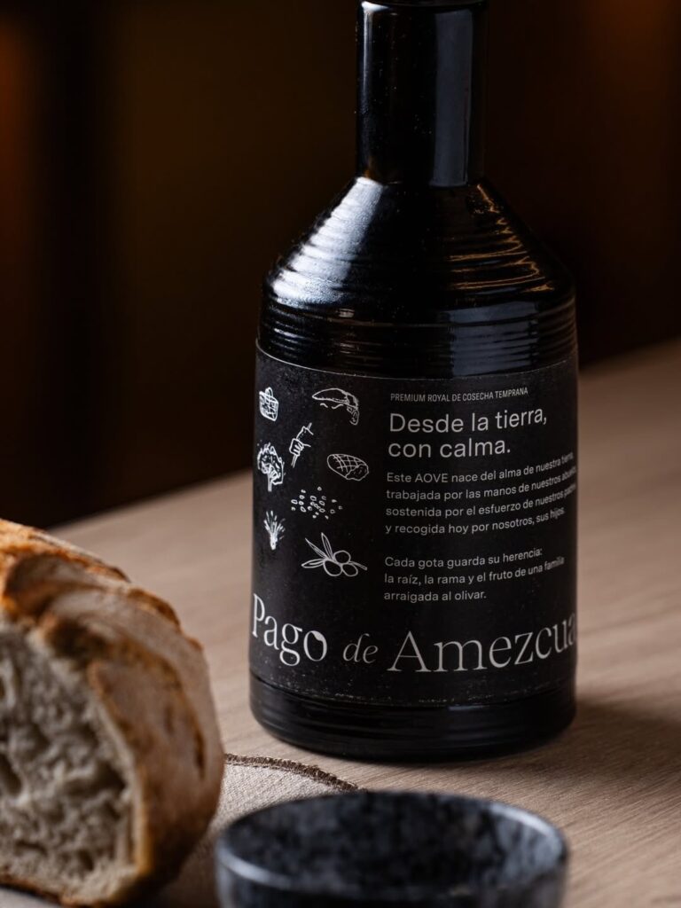 Botella verde de AOVE Pago de Amezcua sobre mesa Gourmet con pan y aceite