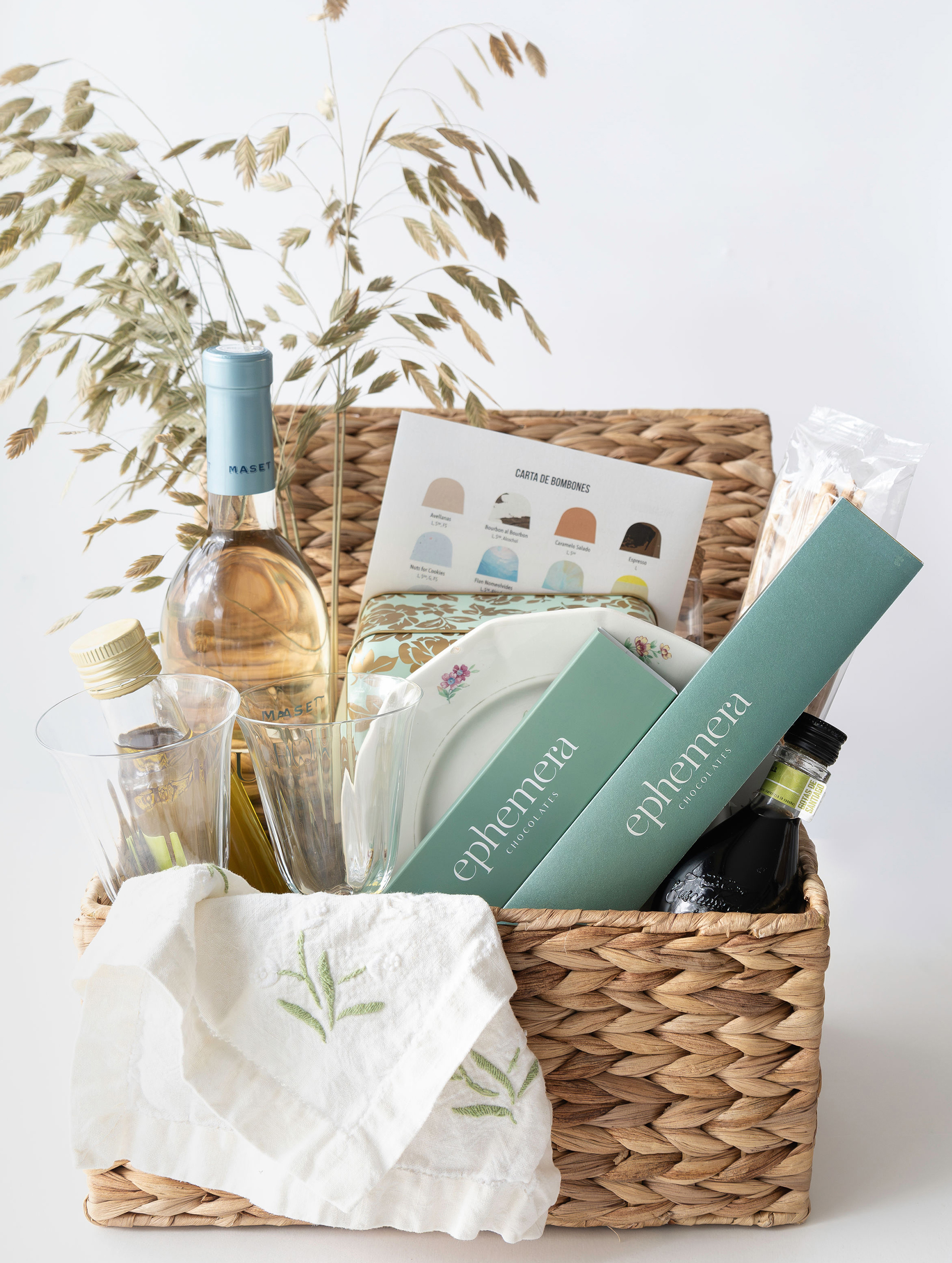 Cesta regalo gourmet con chocolates Ephemera, vino y accesorios de picnic en estilo editorial.