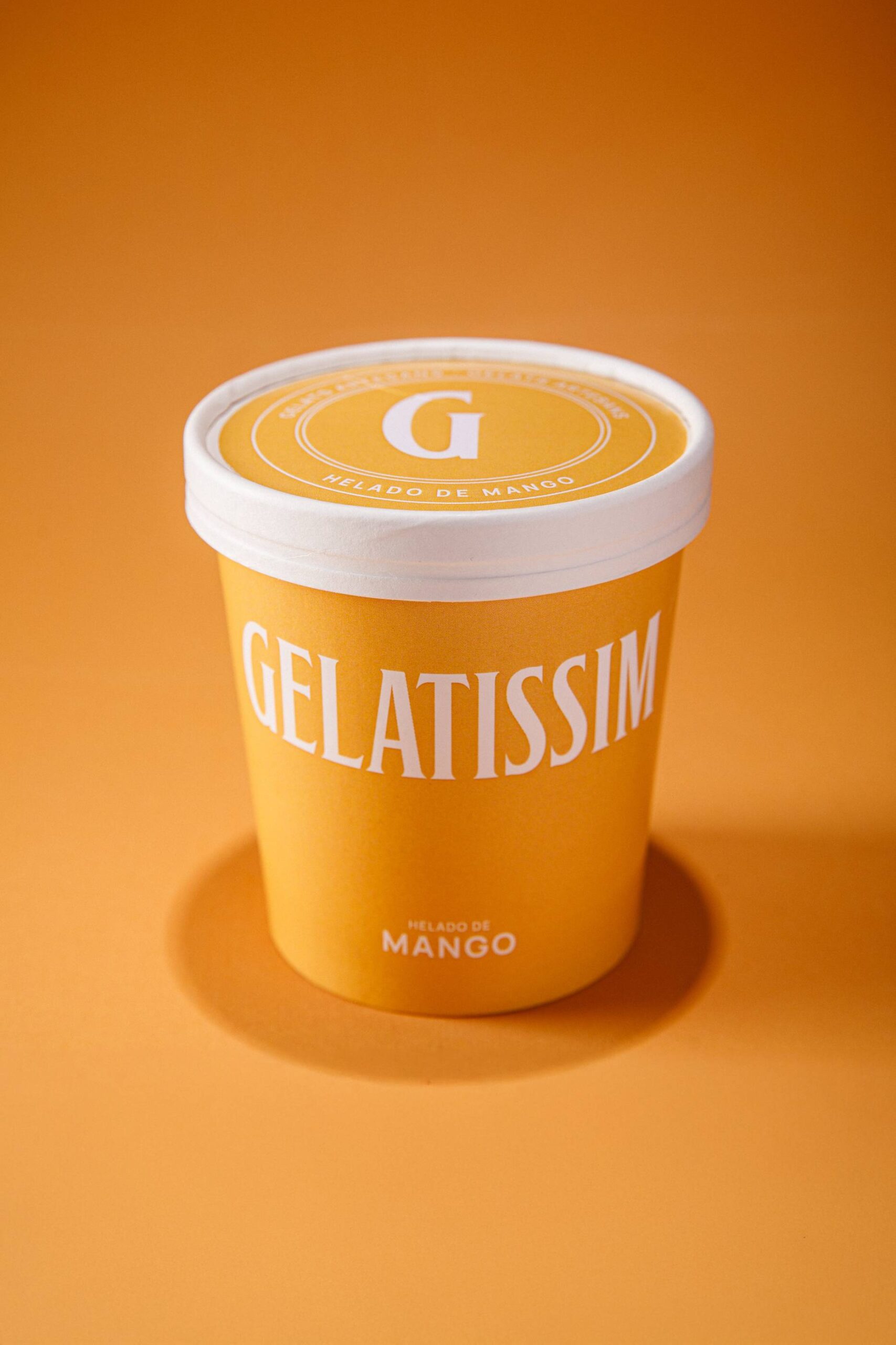 Tarrina de helado de mango Gelatissim sobre fondo naranja.