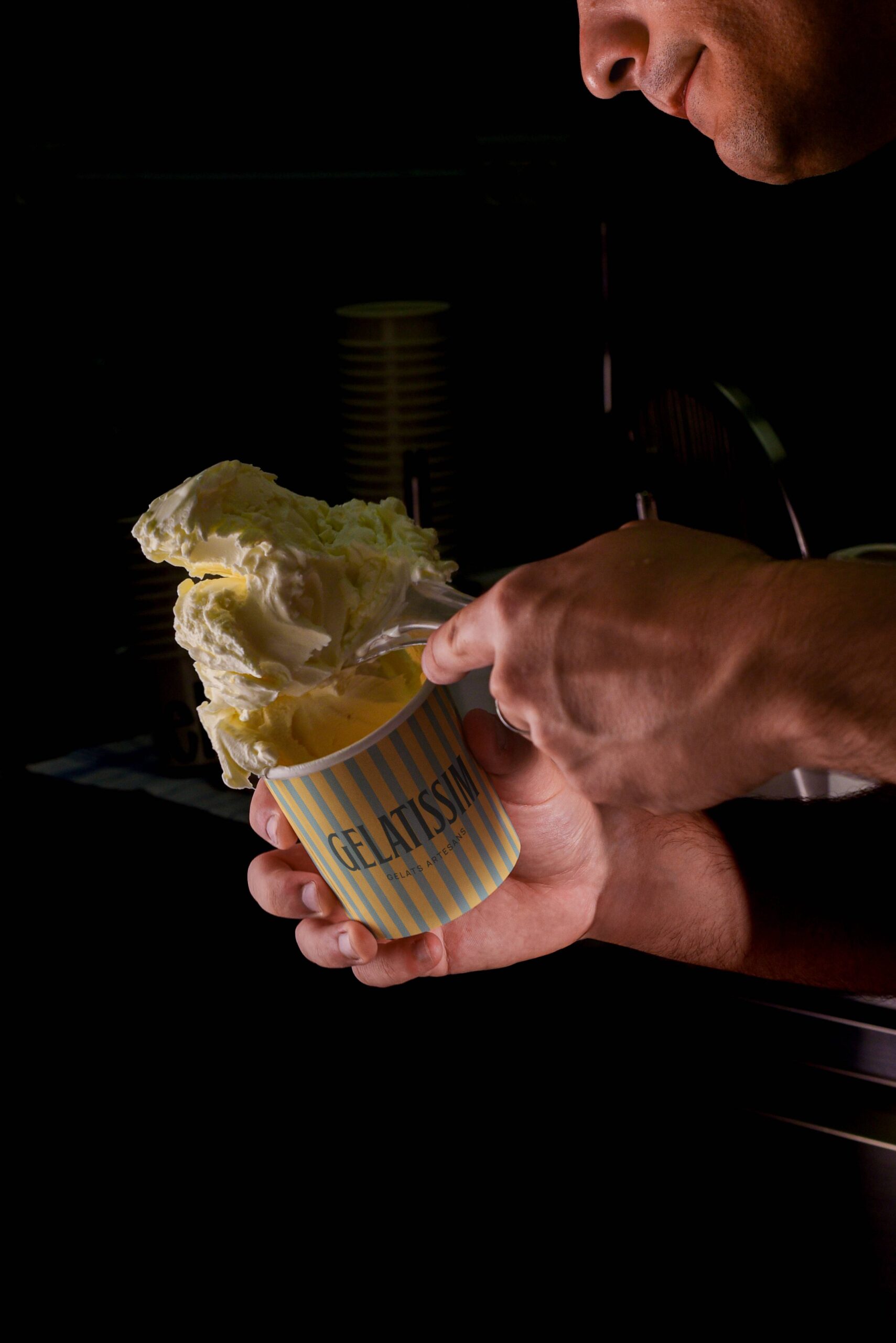Persona sirviendo helado artesanal Gelatissim en vaso de rayas.