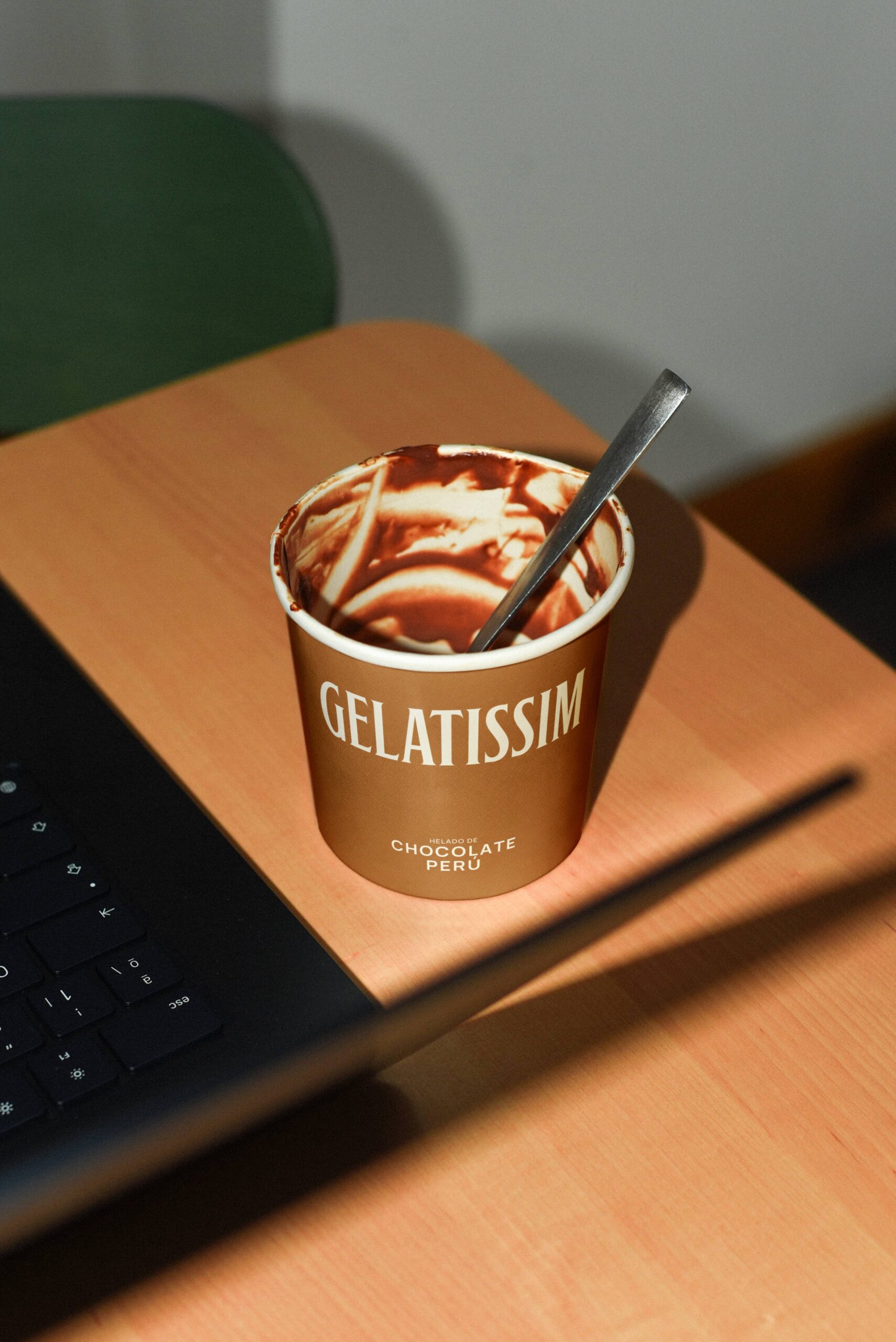 Tarrina vacía de helado de chocolate Perú Gelatissim con cuchara sobre mesa de madera