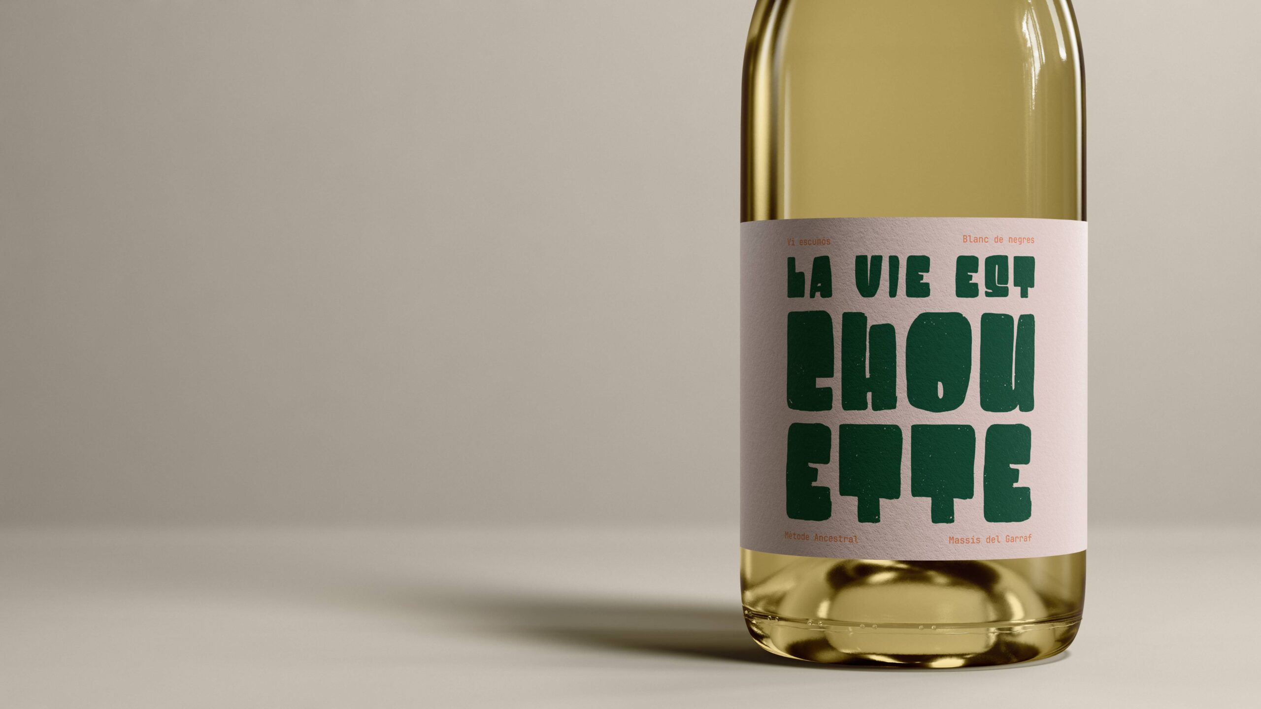 Botella de vino espumoso La Vie Est Chouette con diseño de etiqueta tipográfica minimalista y fondo neutro.