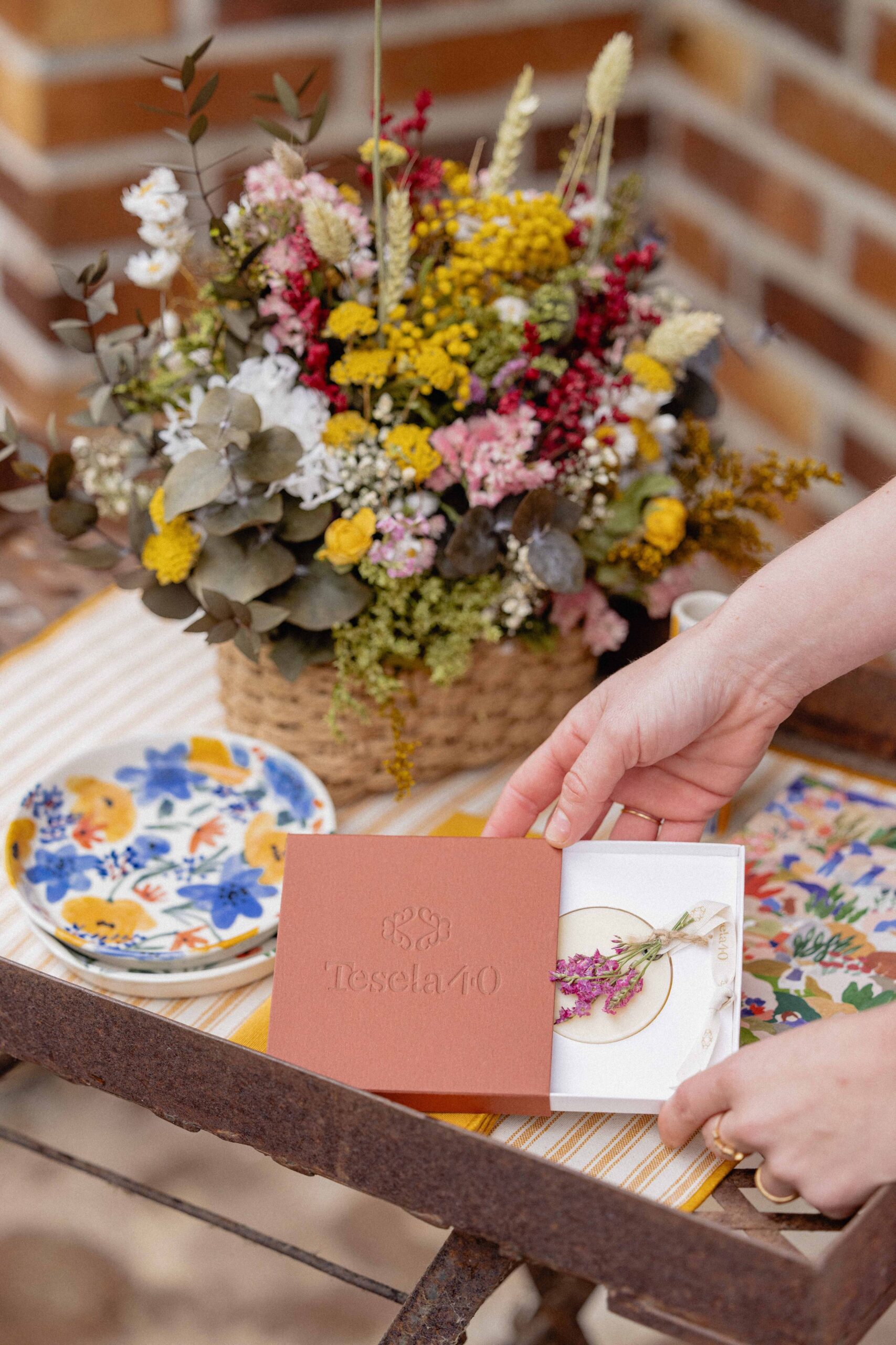 Primer plano de manos abriendo un estuche de cartón color terracota con logotipo grabado, mostrando el cuidado detalle del packaging interior.
