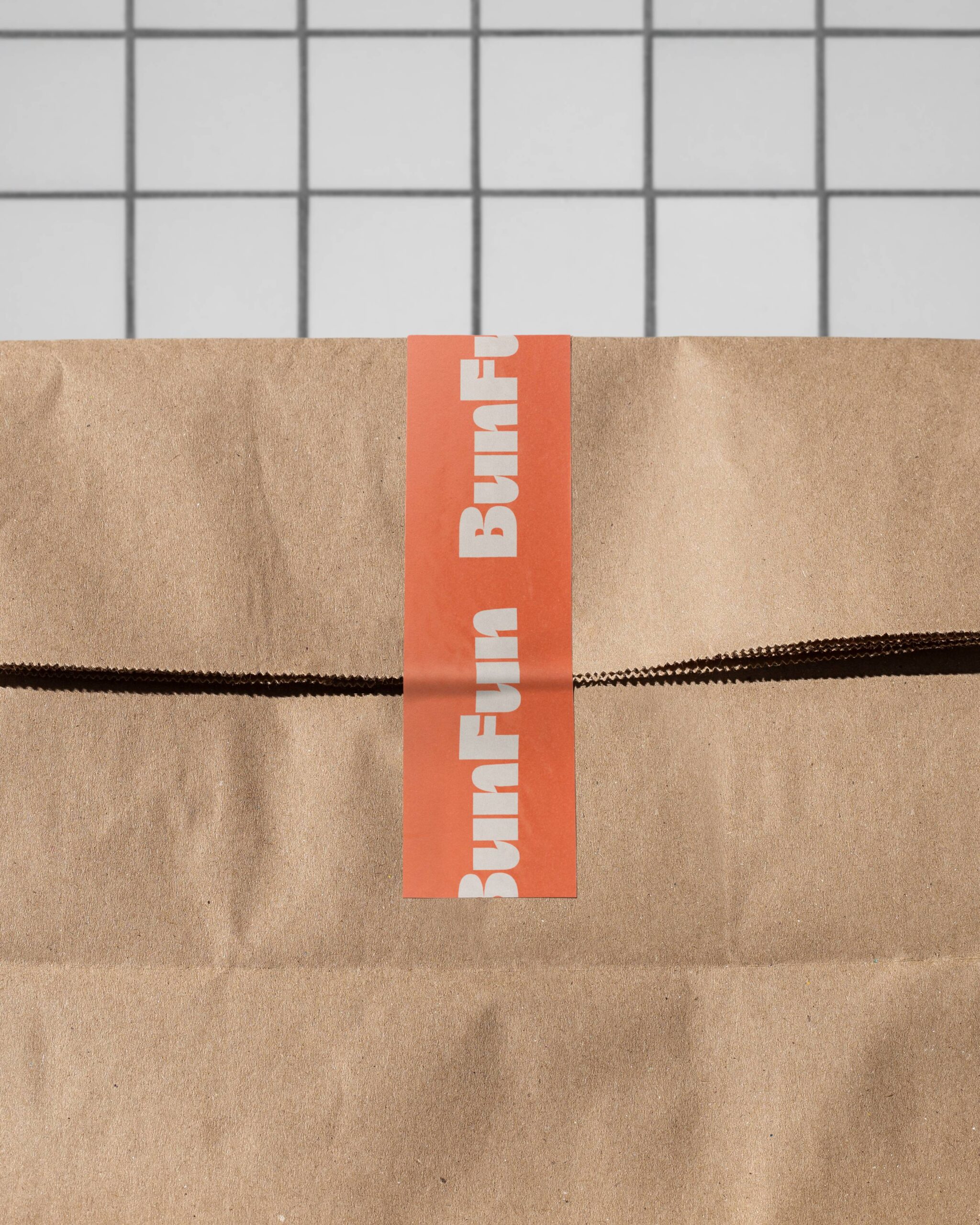 Packaging de delivery: detalle de bolsa de papel kraft cerrada con una faja de seguridad naranja personalizada con el nombre de la marca.
