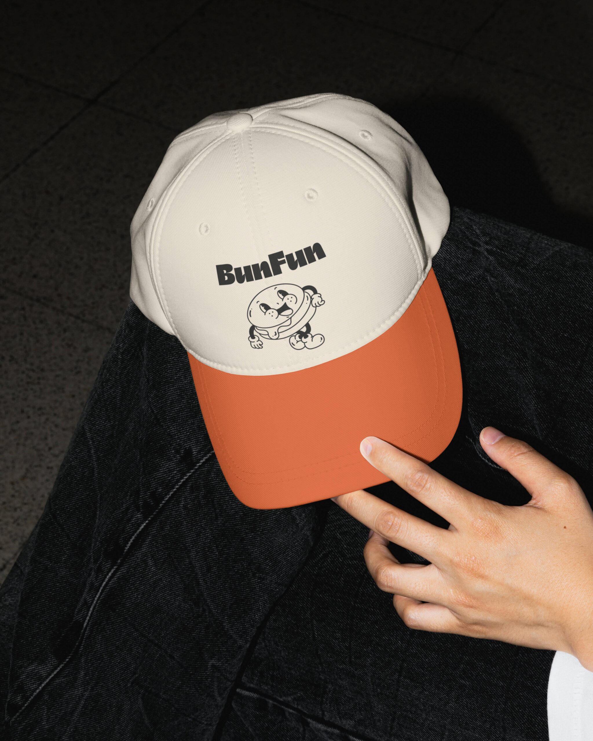 Merchandising de marca: gorra de dos colores con el logotipo y la mascota de BunFun, una hamburguesa con estética de dibujo animado de los años 30.
