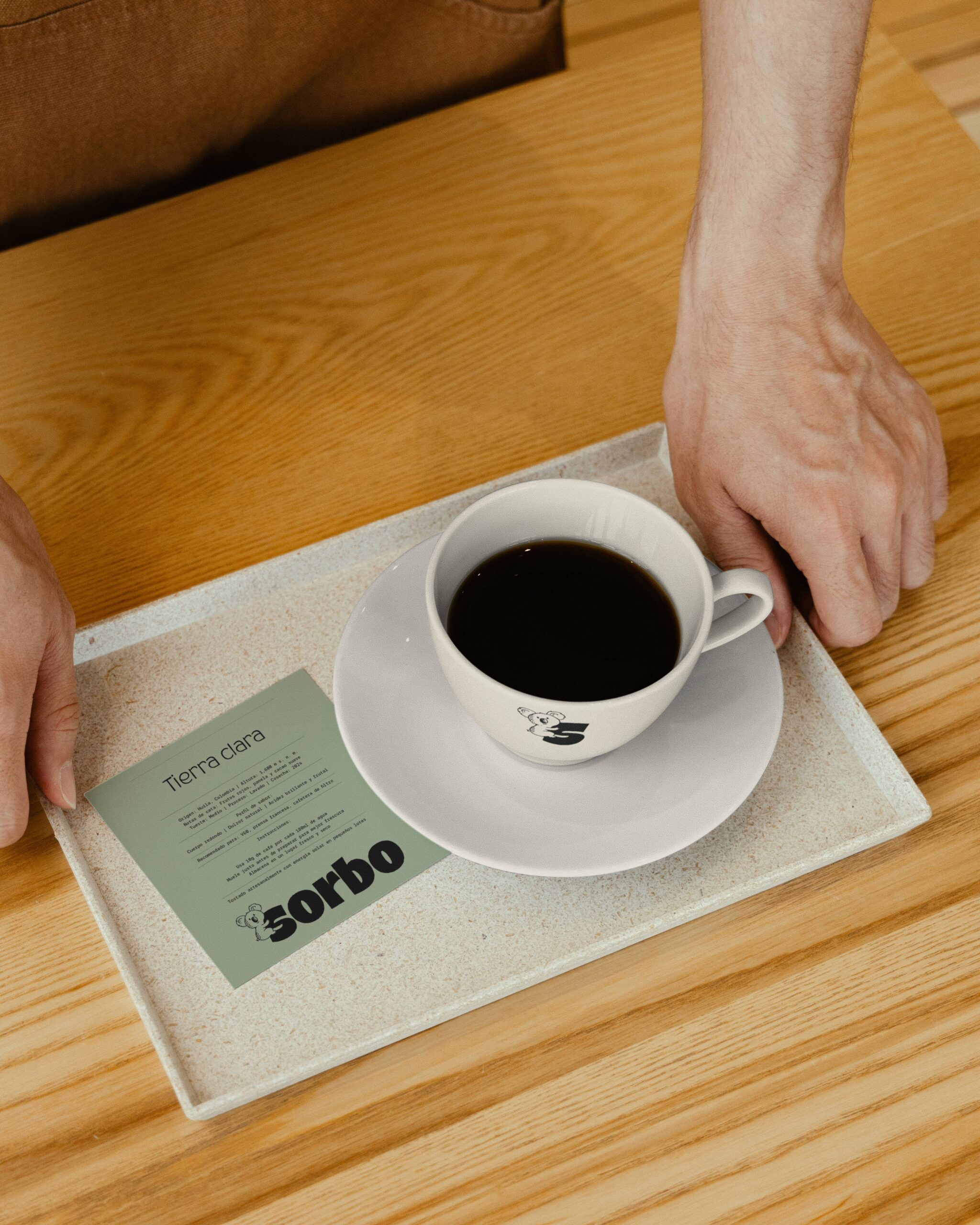 Servicio de café: manos sosteniendo una bandeja con una taza de café solo y una tarjeta técnica informativa de la variedad "Tierra Clara".