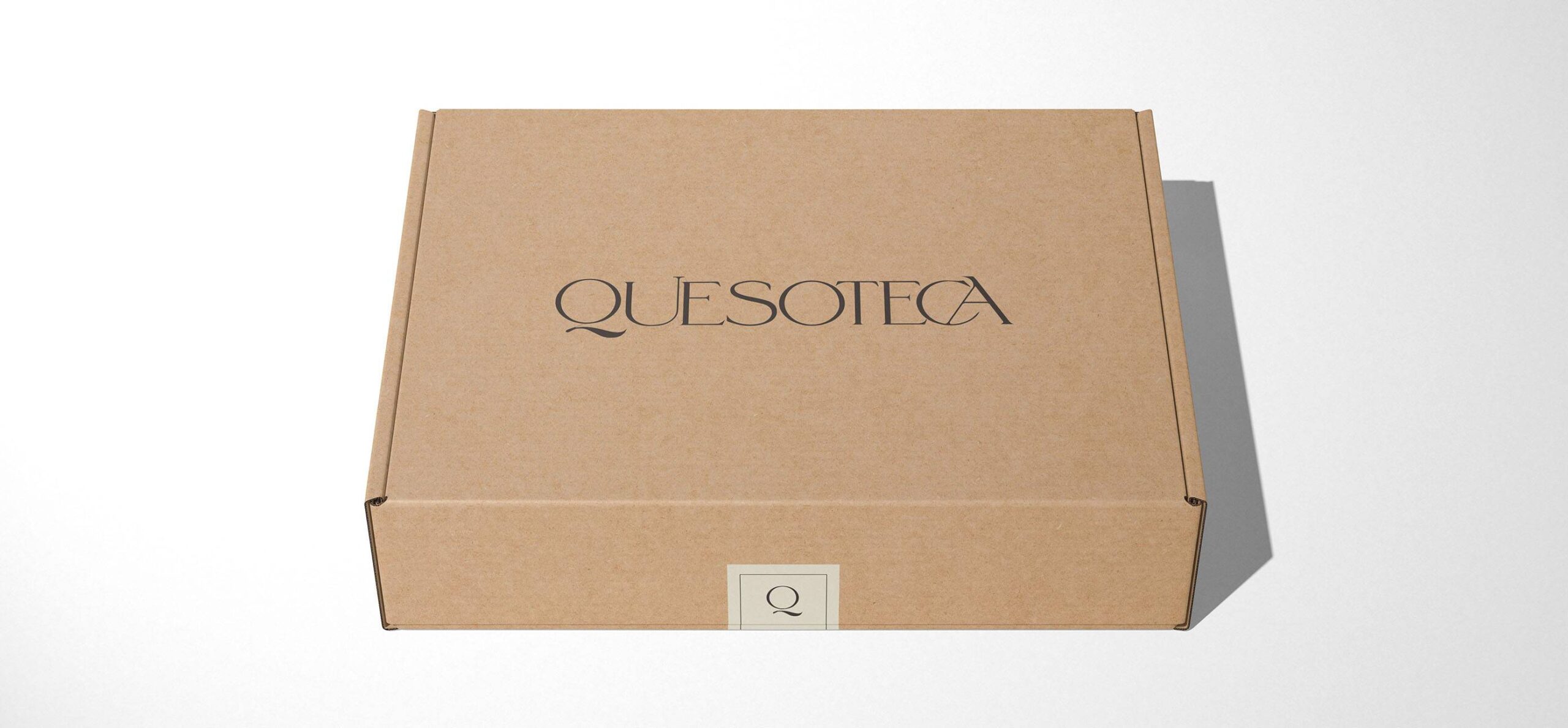 Packaging de e-commerce: caja de cartón kraft para envío a domicilio con el logotipo de Quesoteca impreso en el centro y sello de cierre de seguridad.